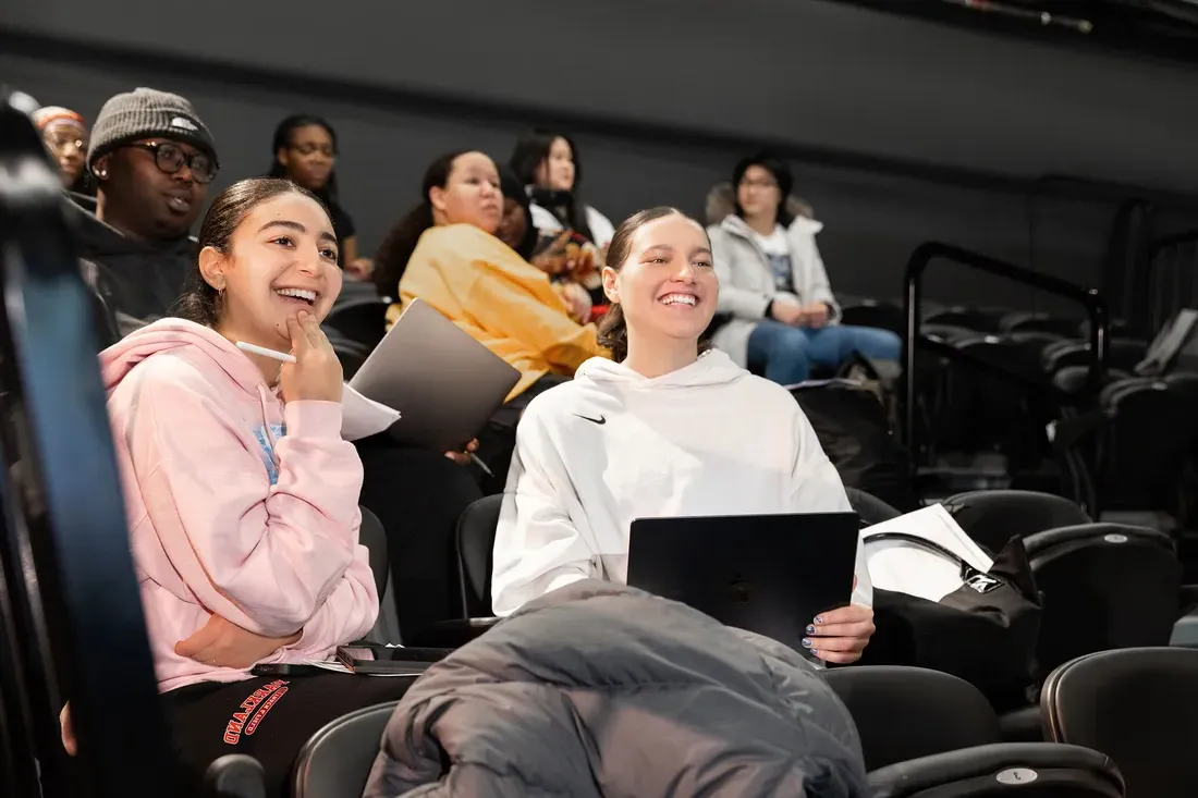 Two students sitting and smiling in Professor Tanisha Jackson's classroom.